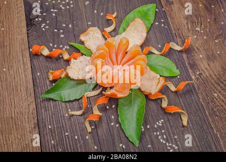 Orange radial geschält wie eine Blume auf Holzhintergrund. Tangentiale Früchte teilweise geschält gereinigt Stockfoto