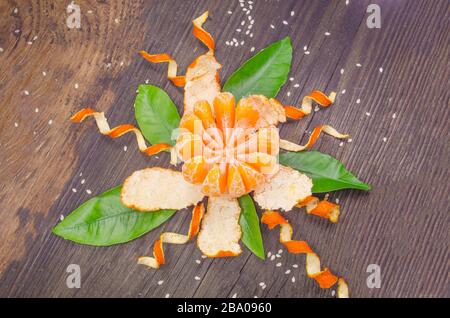 Orange radial geschält wie eine Blume auf Holzhintergrund. Stockfoto
