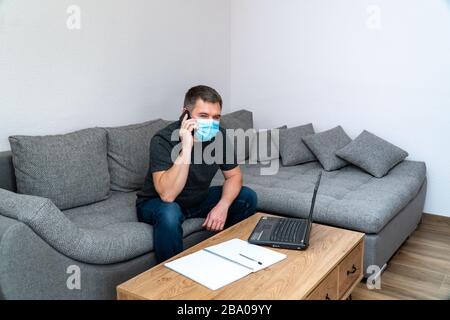 Quarantäne Coronavirus COVID19-Distanzjob. Junger Geschäftsmann, der mit einem Smartphone spricht und mit einem Laptop sitzt. Freie Mitarbeiter im Büro Stockfoto