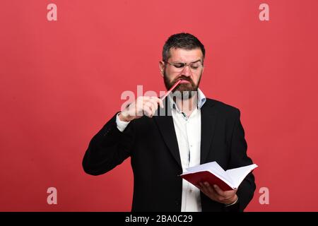 Geschäftsmann mit ernsthaftem und konzentriertem Gesicht und Brille auf rotem Hintergrund. Typ mit offenem Notizbuch und Stift. Erfolgskonzept, Business- und Brainstorming-Konzept. Mann im klassischen Anzug mit Bart hält rotes Buch Stockfoto