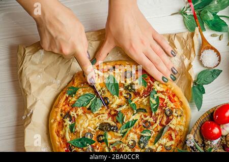 Womans Hand mit Messer schneiden die Pizza. Schneiden von Pizza aus nächster Nähe. Schneiden von Pizza auf Scheiben Stockfoto