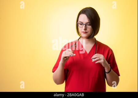 Porträt der schönen Frau Doktor mit Stethoskop mit roten Schruben, ordnet ihr Stethoskop auf einem gelb isolierten Hintergrund. Stockfoto