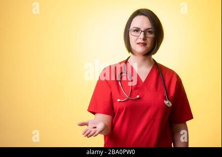 Porträt der schönen Frau Doktor mit Stethoskop mit roten Schruben, die rote Pillen auf der Hand zeigen, die auf einem gelb isolierten Hintergrund posieren. Stockfoto