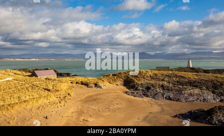 Ein Blick auf Twr Bach, das Rettungsboothaus und die schneebedeckten Snowdonia Berge von Llanddwyn Insel, Anglesey Stockfoto