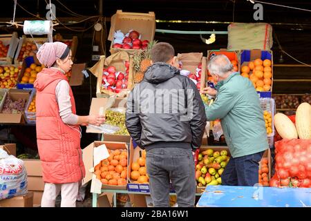 Touristen und Führer, die frisches Obst auf dem Festmarkt in der Nähe von Bishkek, Kirgisistan in Zentralasien auswählen. Lokale Asien-Frau, die für Ausländer verkauft. Stockfoto