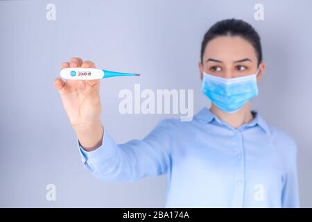 COVID-19 Pandemie Coronavirus Mask Fever Sorry Girl Temperaturprüfung mit Thermometer zu Hause Symptom von SARS-COV-2. Mädchen mit Maske auf Gesichtsscheck Stockfoto