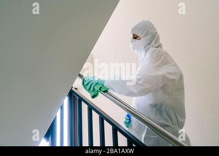 Eine Person, die eine Maske, Handschuhe und einen Sicherheitsanzug trägt, reinigt und desinfiziert eine Tür einer Gemeinschaftswohnung angesichts einer Virus-Pandemie, einer geschützten Safette Stockfoto