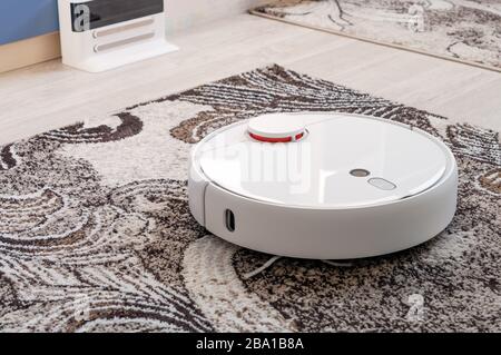Weißer runder Roboter-Staubsauger auf dem Teppichboden Stockfoto