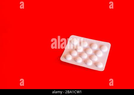 Weiße Blisterpackung mit Aspirin-Tabletten auf rotem Hintergrund.beliebte Medikamente zur Prävention von Schlaganfall und Herzinfarkt.Kopieren Sie Raum und keine Menschen.Überzähler Stockfoto
