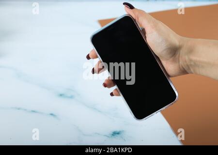 Schwarzes Smartphone in der Hand einer auf Blau isolierten Frau Stockfoto