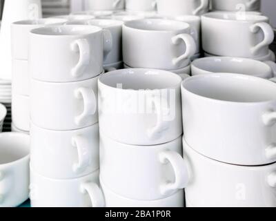 Belichtet auf Stapeln von weißen, sauberen Keramikbechern und Untertöpfen. Die Gerichte im Restaurant werden für Teetrinken und Kaffeetrinken zubereitet. Stockfoto