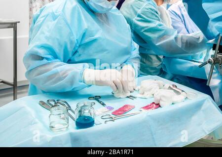 Sterile chirurgische Instrumente und Glasbehälter mit Lösungen auf dem Tisch während einer Operation. Über dem Tisch befinden sich die Hände eines Chirurgen Stockfoto