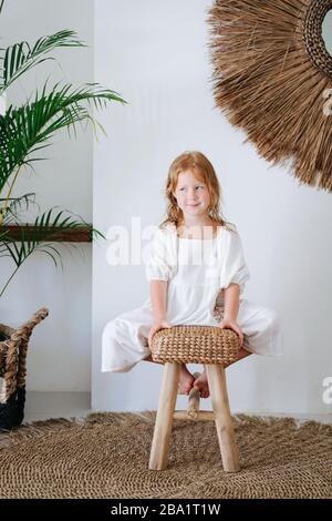 Wunderbares kleines Mädchen mit Rotkopf, das auf einer Bank sitzt und die Füße darunter berühren Stockfoto