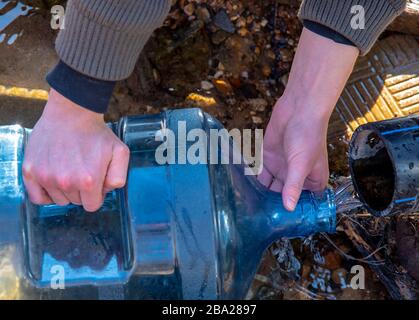 Die Hände der Männer füllen eine Plastikflasche mit Wasser aus einer Feder. Stockfoto