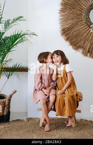 Klatschende Mädchen gleichen Alters sitzen auf einer Korbbank in einem Raum Stockfoto