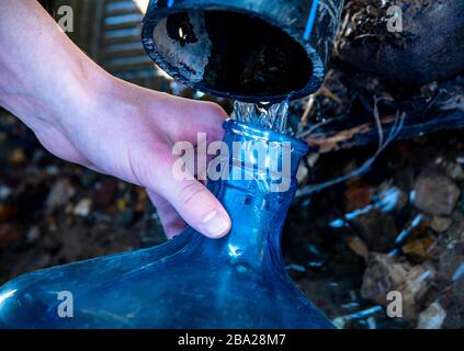 Die Hände der Männer füllen eine Plastikflasche mit Wasser aus einer Feder. Stockfoto