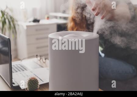 Freiberuflerin verwendet einen Hausbefeuchter am Arbeitsplatz im Heimbüro mit Laptop und Dokumenten. Stockfoto