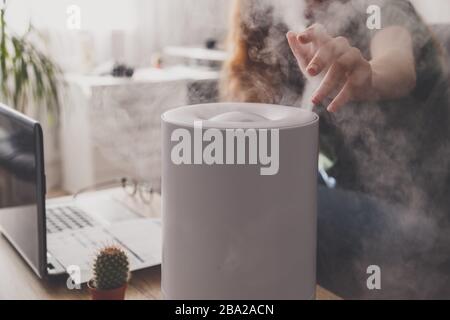 Freiberuflerin verwendet einen Hausbefeuchter am Arbeitsplatz im Heimbüro mit Laptop und Dokumenten. Stockfoto