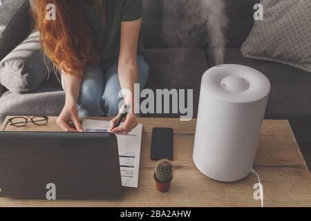 Freiberuflerin verwendet einen Hausbefeuchter am Arbeitsplatz im Heimbüro mit Laptop und Dokumenten. Stockfoto