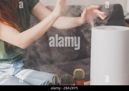 Gesunde Luft. Der Luftbefeuchter verteilt Dampf im Wohnzimmer. Frau übergibt Dampf Stockfoto