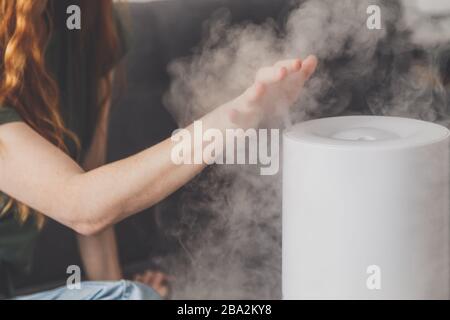 Gesunde Luft. Der Luftbefeuchter verteilt Dampf im Wohnzimmer. Frau übergibt Dampf Stockfoto