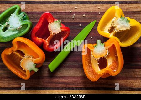 Gelbe, orange-grüne und rote Paprika mit Trennmesser auf einem Holzschneidbrett Stockfoto