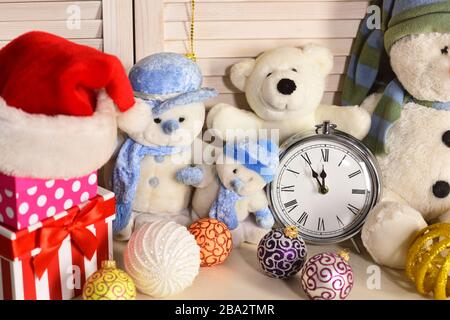 Spielzeug auf Holzwandhintergrund. Schneemänner, Teddybären, Weihnachtsbälle und Präsentkästen in der Nähe des Weckers. Weihnachtsdekoration im Festsaal. Celebration und Neujahrsdekor Stockfoto