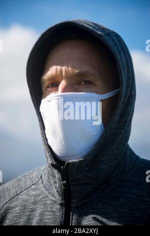 Porträt eines ernsthaften reifen Mannes in einer Kapuze, die eine chirurgische Maske trägt, die im Freien auf Quarantäne vor der Coronavirus-Epidemie steht Stockfoto