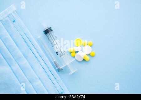 Gelbe Pillen, Kapseln, Tabletten, Spritze und Nadel, eine blaue Gesichtsmaske auf blauem Hintergrund. Beenden Sie das Konzept von Coronavirus. Schützen Sie sich. Stockfoto