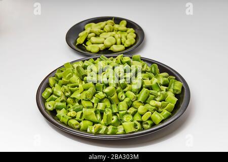 Breite Bohnen in zwei schwarzen Gerichten auf weißem Hintergrund geschnitten Stockfoto