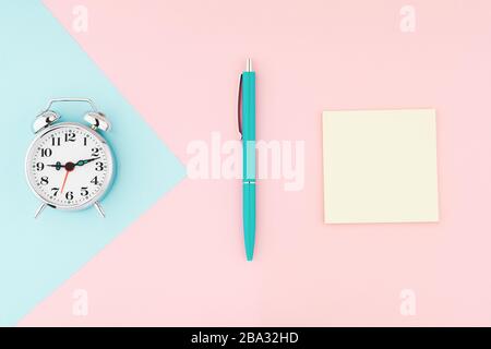 Vintage-Wecker aus Metall mit Bürostift und gelben Haftnotizen auf farbenfrohem Papierhintergrund. Arbeits- und Planungszeit flaches Laienkonzept Stockfoto