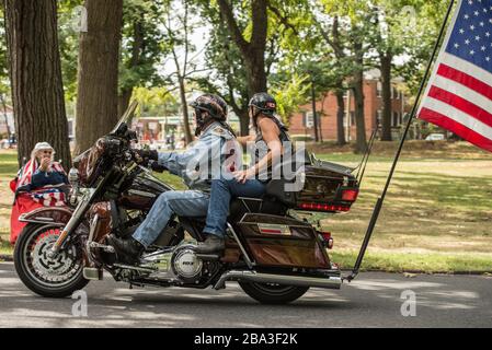 Rolling Thunder Members auf einem Motorrad mit einer großen Flagge, die angebracht ist, bei einer Vietnam-Veteranen-Kundgebung. Im Hintergrund sitzt eine Mutter aus Gold Star. Stockfoto