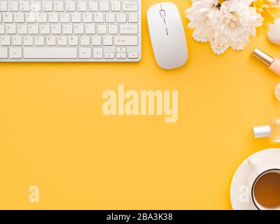 Tastaturmaus, Tasse Tee und knöcherne Blumen, Schminkwerkzeuge und Kosmetikprodukte in seiner Nähe isoliert auf einem gelben Hintergrund. Flacher Lay, Draufsicht, Kopierspac Stockfoto