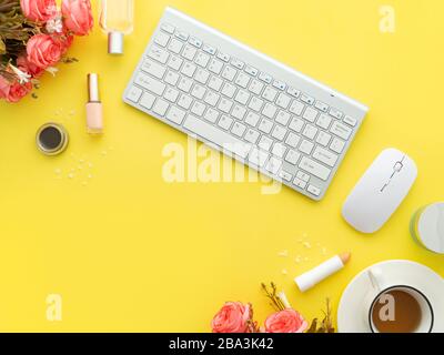 Tastaturmaus, Tasse Tee- und Schminkwerkzeuge und Kosmetikprodukte rund um sie isoliert auf einem gelben Hintergrund. Flaches Layout, Kopierbereich in der Draufsicht. Feminin Stockfoto