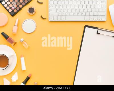 Tastaturmaus, Tasse Tee- und Schminkwerkzeuge und Kosmetikprodukte rund um sie isoliert auf einem gelb-orangefarbenen Hintergrund. Flaches Layout, Kopierbereich in der Draufsicht. Fe Stockfoto