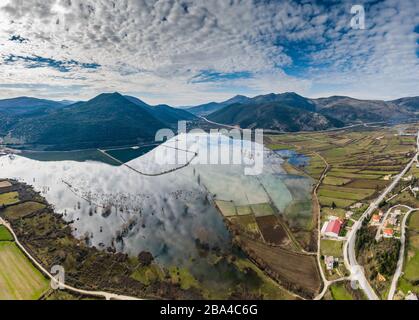 Flug über das überschwemmte Tal in Griechenland. Die überfluteten Felder, Straßen, Berge im Hintergrund, die bewohnte Siedlung. Reflexion der Berge in Stockfoto