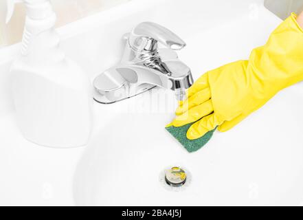 Frau in gelben Gummihandschuhen ist die Reinigung des Badezimmerwaschkörpers mit Waschmittel und Schwamm Stockfoto