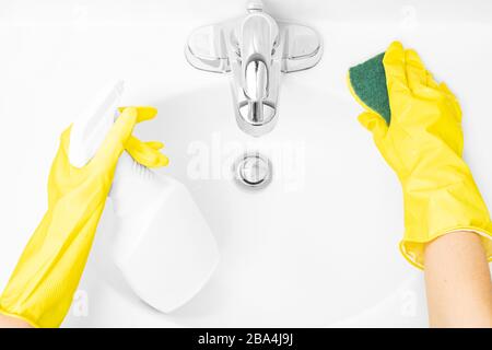 Frau in gelben Gummihandschuhen ist die Reinigung des Badezimmerwaschkörpers mit Waschmittel und Schwamm Stockfoto