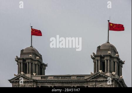 Shanghai, China - 4. Mai 2010: Nahaufnahme der dunkelgrauen Oberseite des AIA-Versicherungsgebäudes mit 2 chinesischen Flaggen unter hellblauem Himmel. Früher, Nordchina Dai Stockfoto