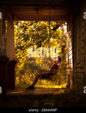 Ein kleiner Junge sitzt auf einer Landvorhalle, die ein verfallenes Bauernhaus in den Ozark Mountains erkundet. Stockfoto