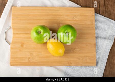 Ganze grüne Äpfel und eine Zitrone auf einem Holzbrett. Draufsicht Stockfoto