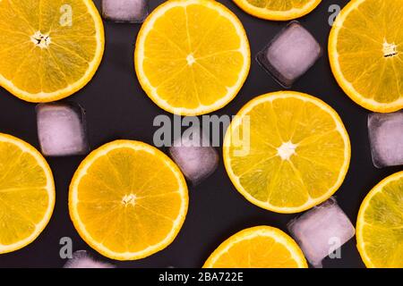 Scheiben von Orange- und Eiswürfeln auf schwarzem Hintergrund. Stockfoto