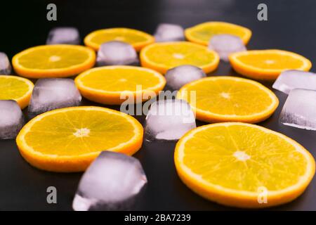 Scheiben von Orange- und Eiswürfeln auf schwarzem Hintergrund. Stockfoto