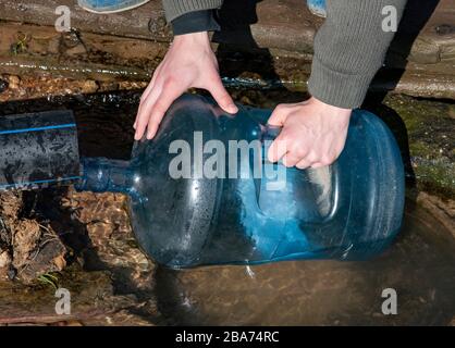 Die Hände der Männer füllen eine Plastikflasche mit Wasser aus einer Feder. Stockfoto