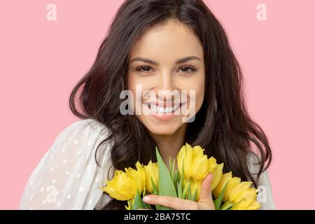 Junge, hübsche dunkelhaarige Frau, die gelbe Blumen hält und lächelt Stockfoto