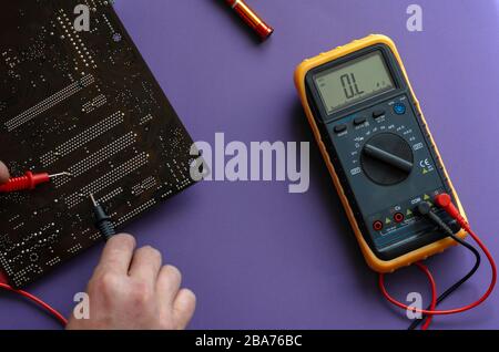 Prüfen des elektrischen Widerstands der Hauptplatine. Die Hände mit einem Digitalmultimeter testen. Ansicht von oben. Selektiver Fokus. Nahaufnahme Stockfoto