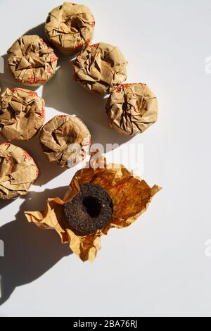 Puerh-Tee in Handarbeit Papierverpackungen auf weißem Hintergrund am sonnigen Tag. Trendige Minimal chinese Drink Konzept Stockfoto