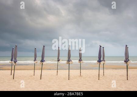 Viele Sonnenschirme am sandigen Strand Hintergrund Meer und schwarze Regenwolken. Stockfoto