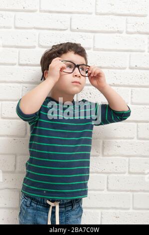 Kleiner Junge in Brille gegen eine Ziegelwand Stockfoto