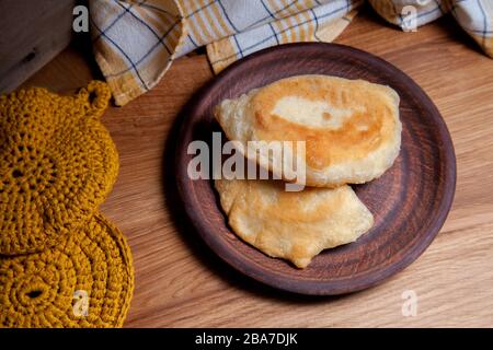 Tonplatte mit zwei einzelnen gebratenen Pasteten mit Fleisch auf Holztisch. Tatarische traditionelle Pasteten. Stockfoto